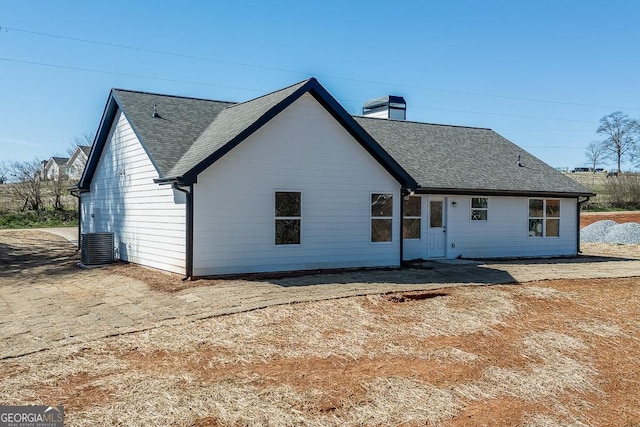 rear view of property featuring a shingled roof, a chimney, and central AC unit