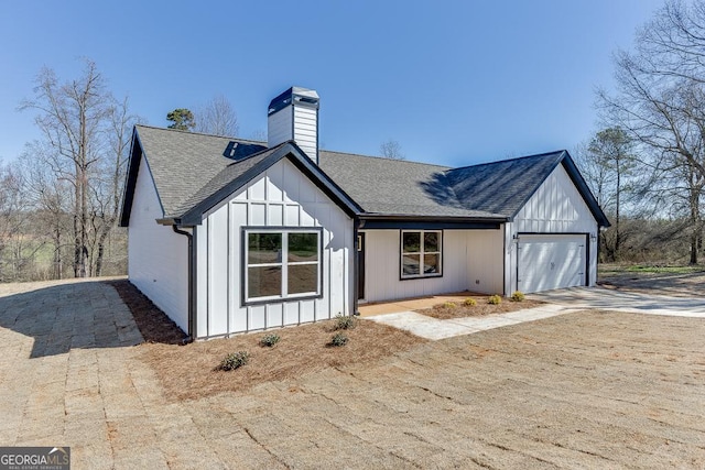 modern inspired farmhouse featuring roof with shingles, a chimney, board and batten siding, a garage, and driveway