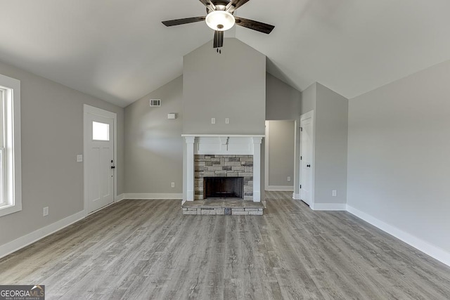 unfurnished living room featuring light wood-type flooring, ceiling fan, baseboards, and a stone fireplace