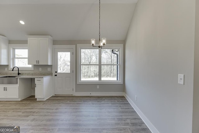 kitchen with white cabinets, light wood-style flooring, decorative light fixtures, light countertops, and a sink