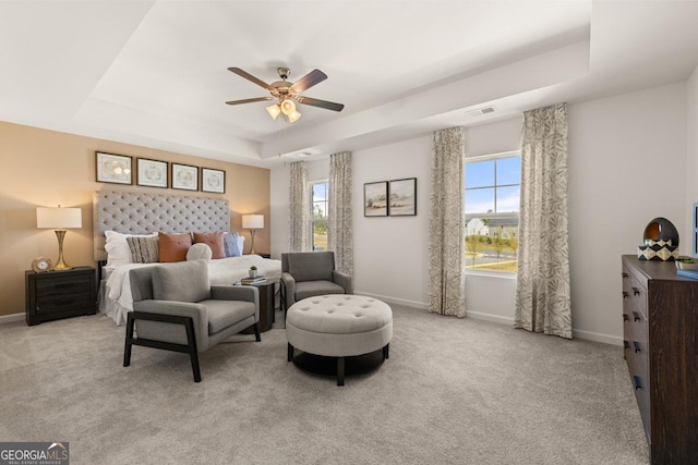 carpeted bedroom with ceiling fan, a raised ceiling, and multiple windows