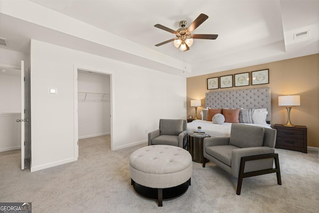 bedroom with light colored carpet, a tray ceiling, a closet, ceiling fan, and a spacious closet