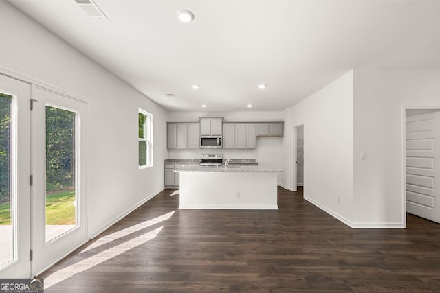 kitchen with a center island with sink, stainless steel appliances, dark hardwood / wood-style flooring, gray cabinets, and light stone counters