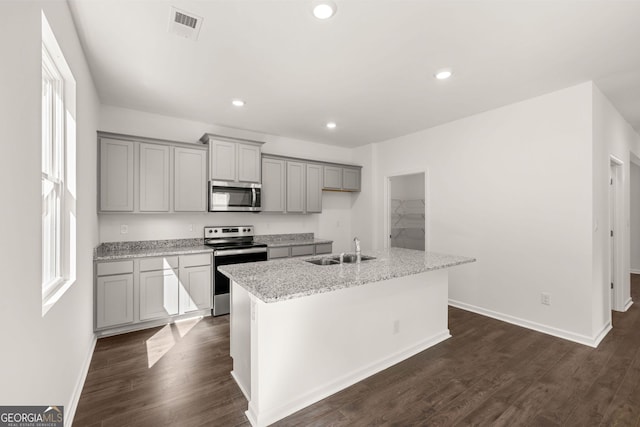 kitchen featuring a center island with sink, appliances with stainless steel finishes, sink, light stone counters, and dark hardwood / wood-style flooring