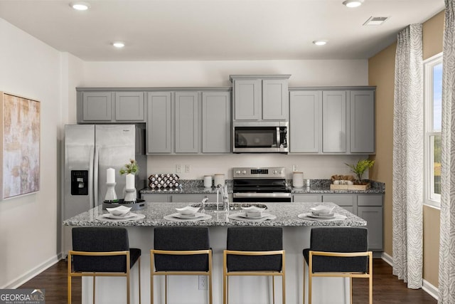 kitchen with gray cabinets, stainless steel appliances, and a center island with sink