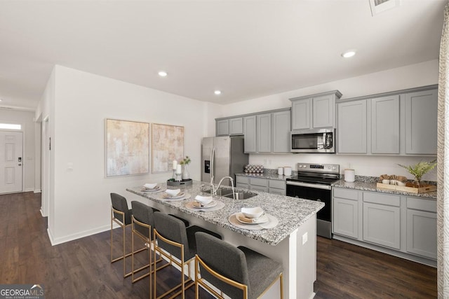 kitchen featuring a center island with sink, sink, a kitchen breakfast bar, stainless steel appliances, and light stone countertops