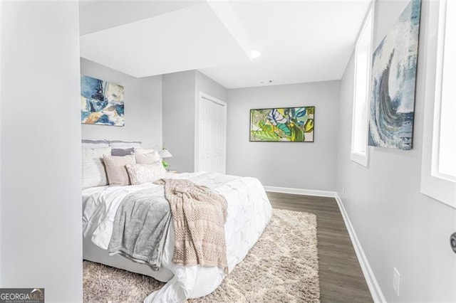 bedroom with a closet, dark wood-style flooring, and baseboards