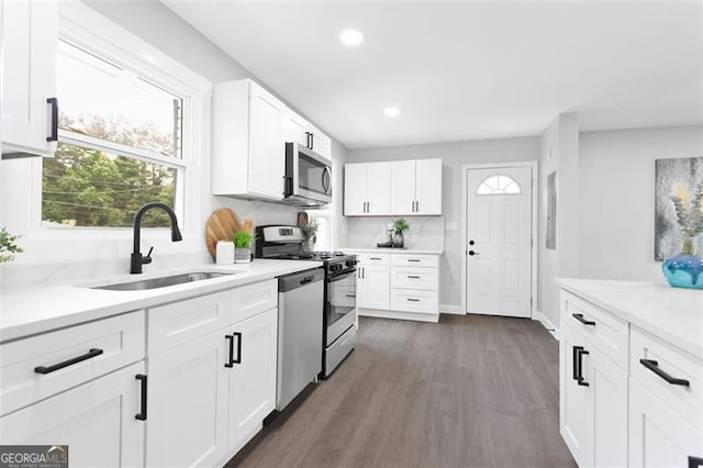 kitchen with stainless steel appliances, a sink, white cabinets, light countertops, and dark wood finished floors