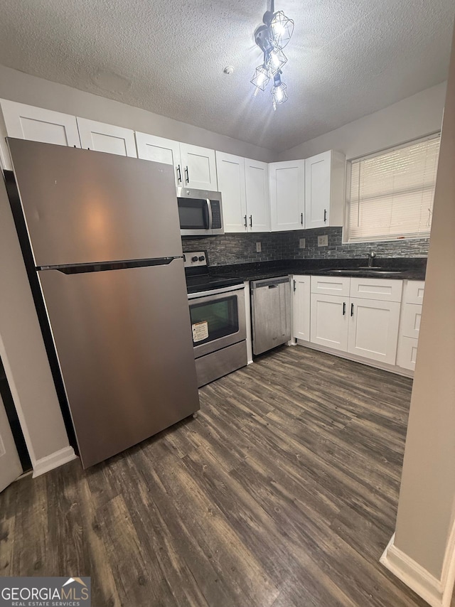 kitchen with sink, backsplash, appliances with stainless steel finishes, white cabinets, and dark hardwood / wood-style floors