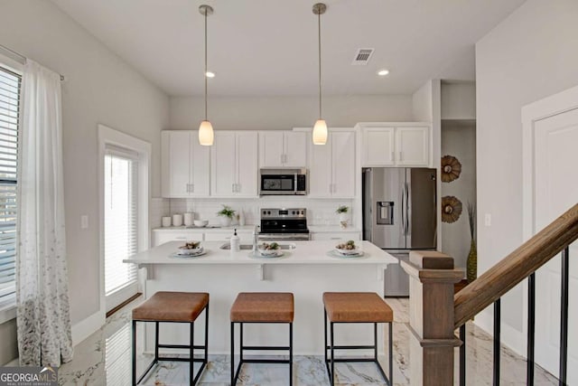 kitchen with stainless steel appliances, an island with sink, light countertops, and white cabinetry