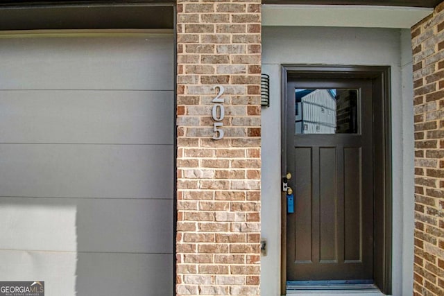 doorway to property featuring a garage and brick siding