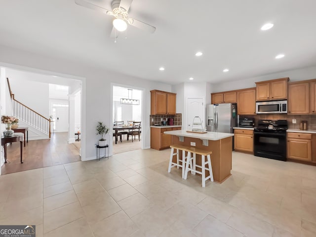 kitchen with a breakfast bar area, light countertops, appliances with stainless steel finishes, decorative backsplash, and an island with sink