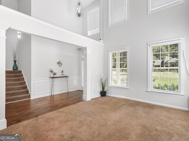 carpeted foyer featuring a notable chandelier, decorative columns, and a high ceiling