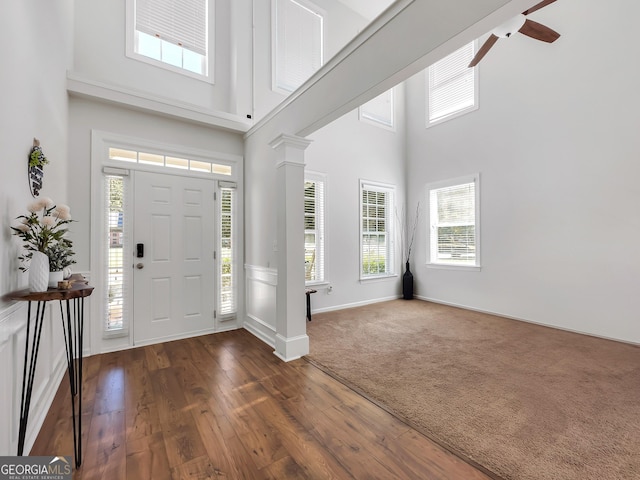 foyer featuring a high ceiling, a ceiling fan, baseboards, dark wood finished floors, and ornate columns