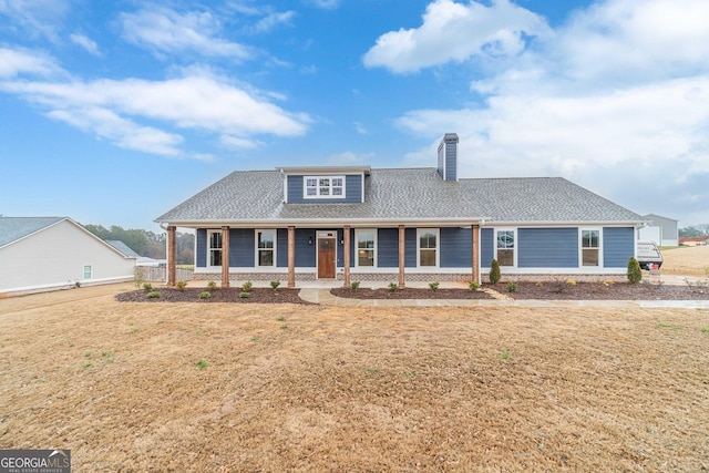 view of front of house with a porch, a chimney, a front yard, and a shingled roof