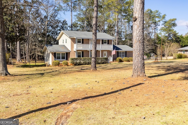 view of front of house featuring brick siding, a front yard, and a balcony