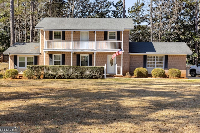 front of property featuring covered porch, brick siding, a balcony, and a front lawn