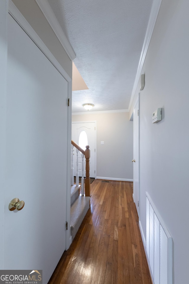 corridor featuring dark wood-style flooring, crown molding, visible vents, baseboards, and stairs