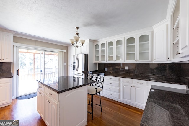 kitchen with a center island, hanging light fixtures, glass insert cabinets, white cabinets, and stainless steel fridge