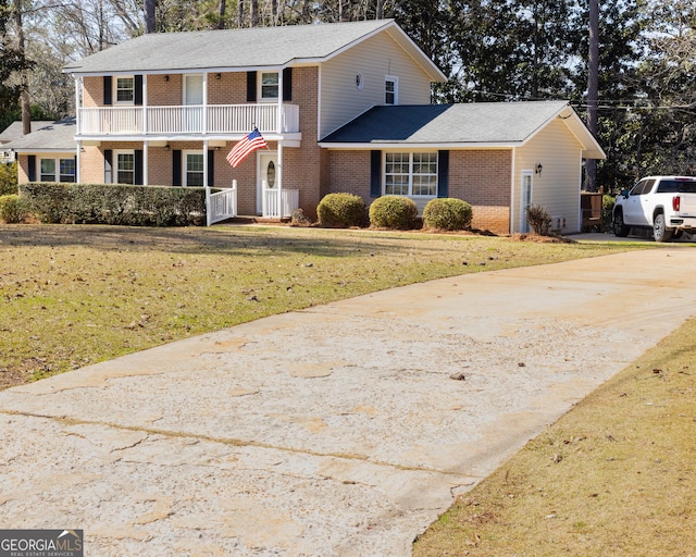 view of front of home featuring driveway, brick siding, a front lawn, and a balcony