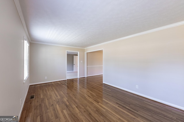 spare room with ornamental molding, dark wood-type flooring, visible vents, and baseboards