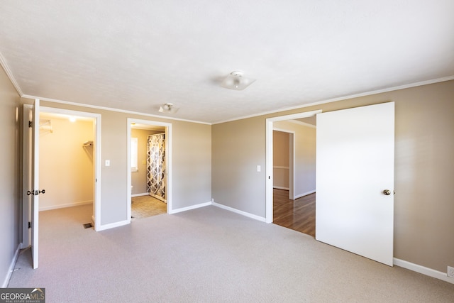 unfurnished bedroom featuring light carpet, ornamental molding, a walk in closet, and baseboards