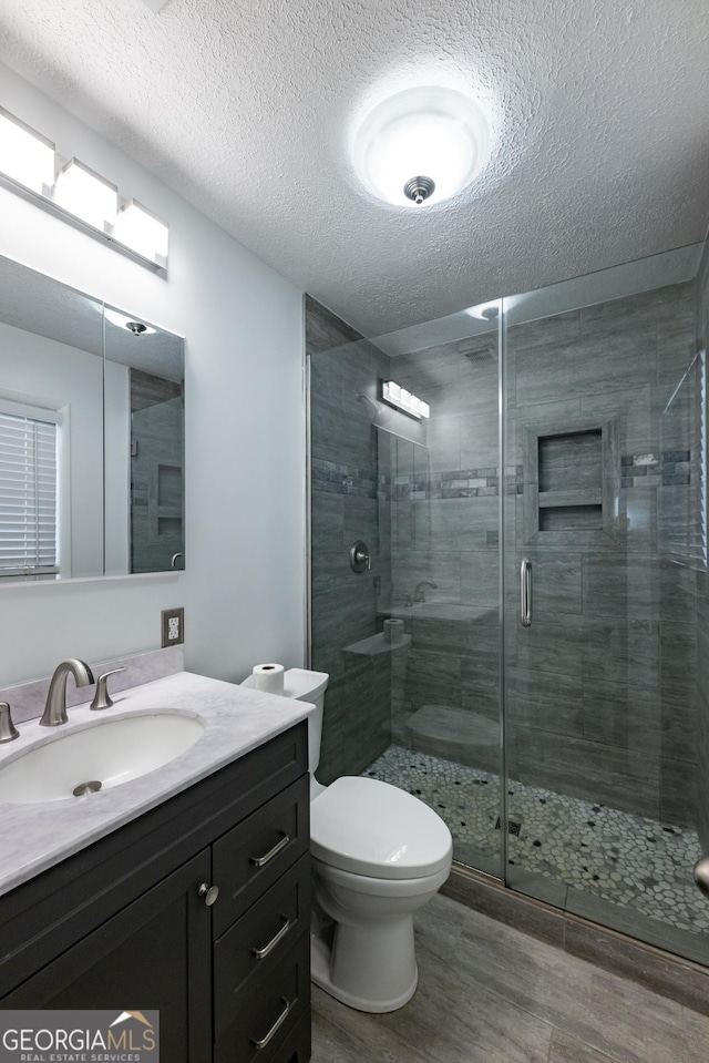 full bath featuring toilet, wood finished floors, a textured ceiling, vanity, and a shower stall