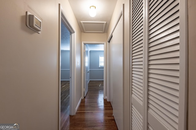 hallway with dark wood-type flooring, attic access, and baseboards