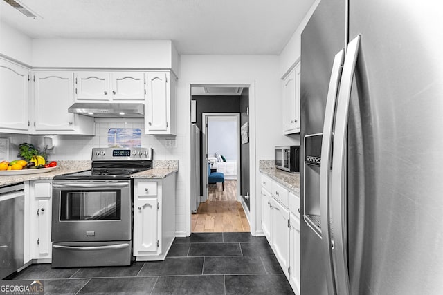 kitchen with tasteful backsplash, stainless steel appliances, dark tile patterned flooring, light stone countertops, and white cabinets