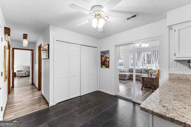 interior space featuring ceiling fan, light stone counters, a textured ceiling, and white cabinets