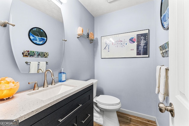 bathroom with toilet, a textured ceiling, wood-type flooring, and vanity