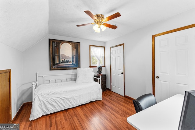 bedroom featuring ceiling fan, vaulted ceiling, wood-type flooring, and a textured ceiling