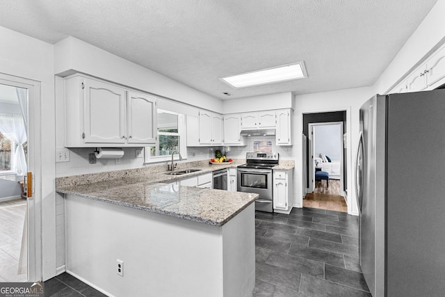 kitchen featuring sink, light stone counters, white cabinetry, stainless steel appliances, and kitchen peninsula