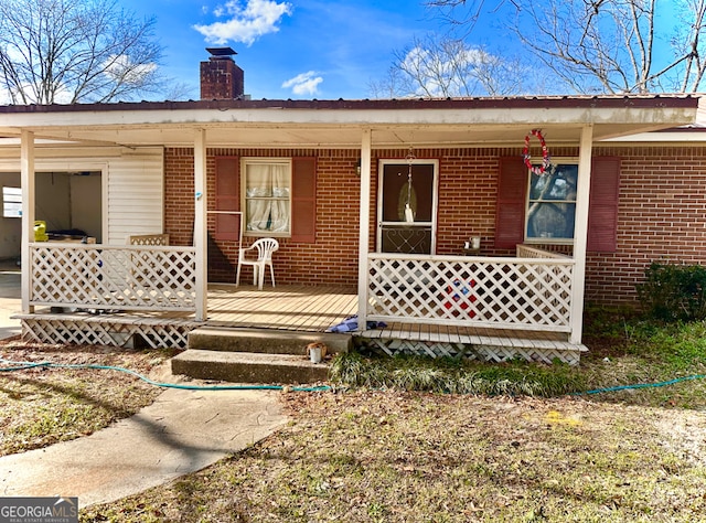 doorway to property with a porch, brick siding, and a chimney