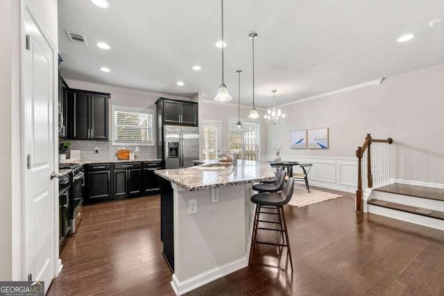 kitchen featuring a kitchen bar, decorative light fixtures, stainless steel appliances, light stone countertops, and a kitchen island with sink