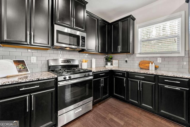 kitchen with light stone counters, stainless steel appliances, dark wood-type flooring, and decorative backsplash