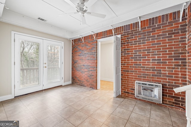 unfurnished living room featuring heating unit, ceiling fan, french doors, and brick wall