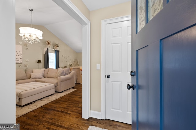 foyer entrance featuring vaulted ceiling, dark wood-type flooring, and a chandelier