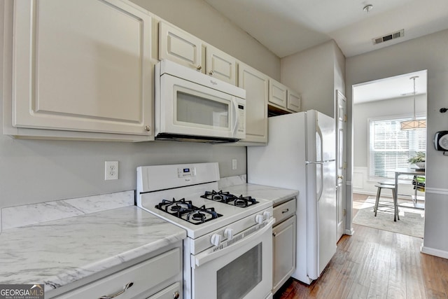 kitchen featuring light stone countertops, visible vents, white cabinets, wood finished floors, and white appliances