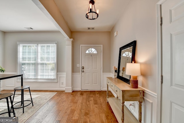 foyer with a wainscoted wall, light wood-style flooring, visible vents, and an inviting chandelier