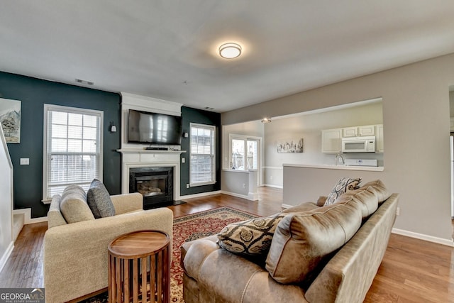 living area with light wood-style flooring, a fireplace, visible vents, and baseboards