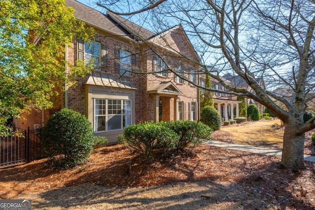 view of front of home featuring roof with shingles, brick siding, and fence