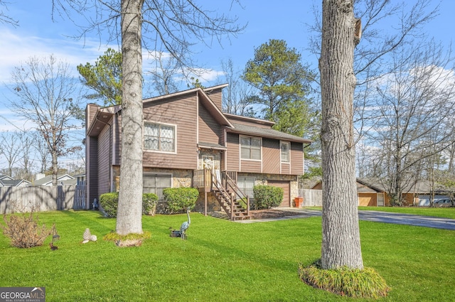 bi-level home featuring driveway, a front lawn, stone siding, and fence