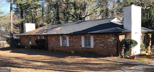 view of side of home featuring roof with shingles, brick siding, and a chimney