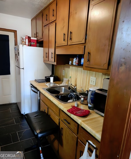 kitchen with light countertops, dishwasher, brown cabinets, a sink, and freestanding refrigerator