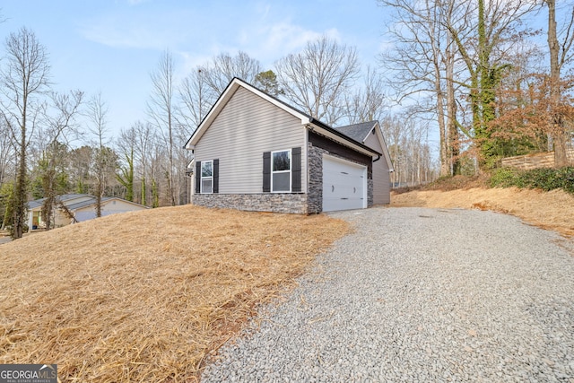 view of home's exterior with gravel driveway, stone siding, and an attached garage