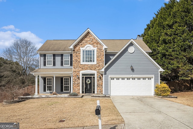 traditional home with driveway, stone siding, a garage, and fence