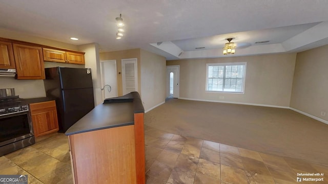 kitchen featuring black fridge, a center island, a raised ceiling, stainless steel gas range oven, and light colored carpet