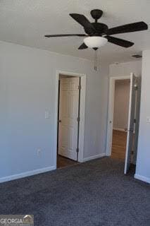 unfurnished bedroom with a ceiling fan, dark carpet, and baseboards