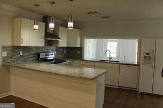 kitchen featuring a peninsula, light stone countertops, wall chimney range hood, and a sink